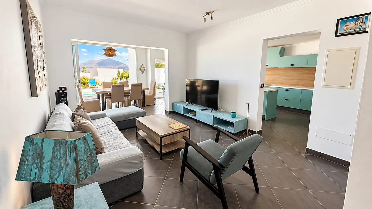 Bright living room with sofa and TV, open to the dining area and terrace